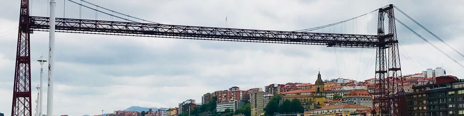 Un puente colgante imponente que cruza un río, con un paisaje urbano de fondo.
