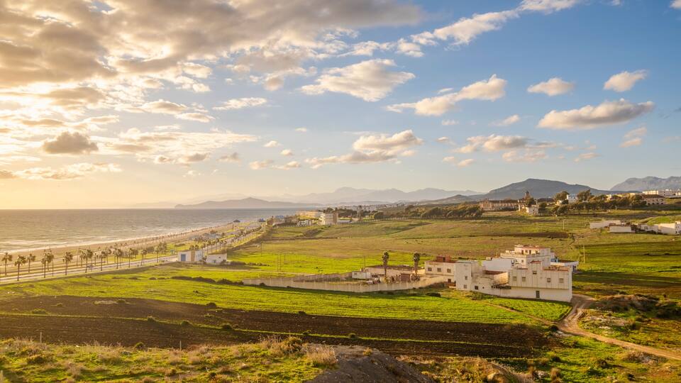 A coastal landscape with a beach, green fields, and a white building.