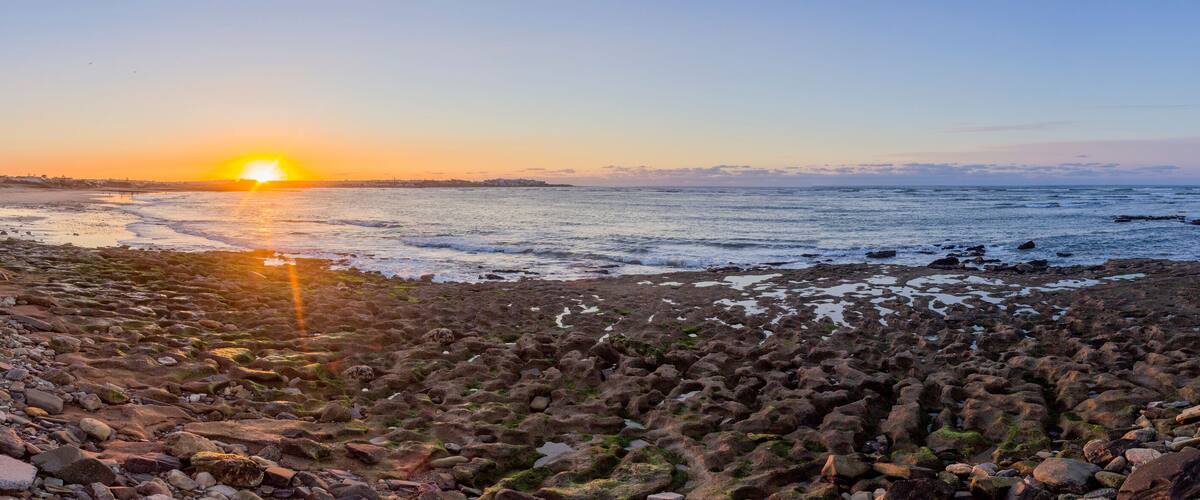 A rocky shoreline at sunset with the sun low on the horizon.