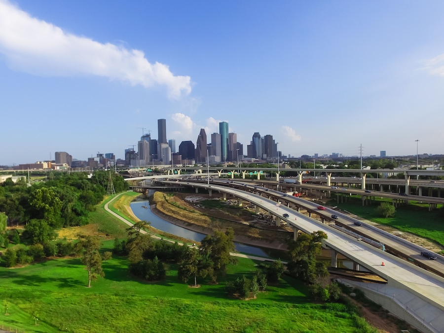 Un horizonte urbano con rascacielos modernos, una autopista con varios carriles y un río que serpentea a través de una zona verde con parque.