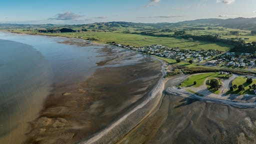 A coastal town with a beach, green fields, and rolling hills in the background.