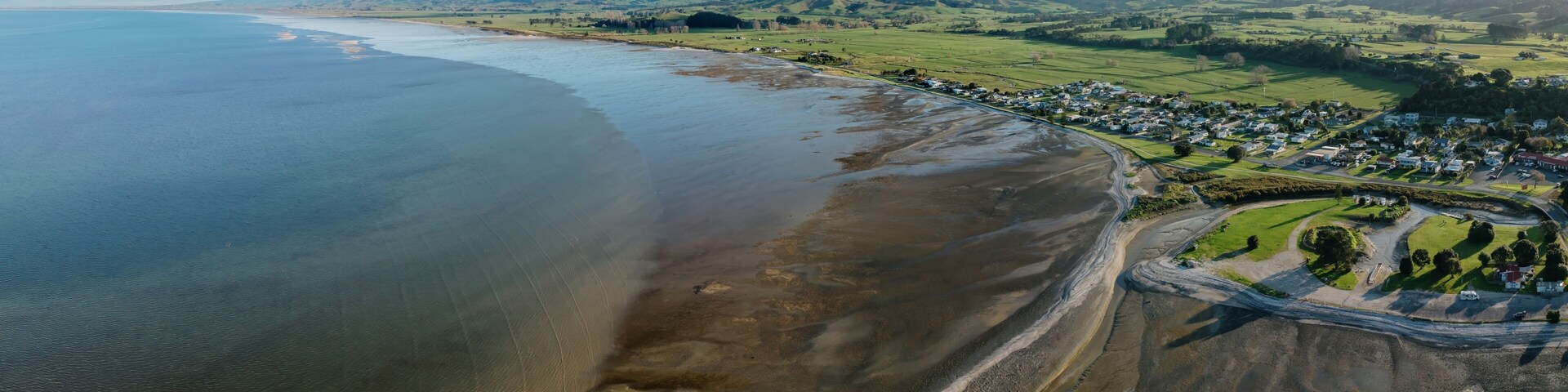 Eine KĂŒstenstadt mit Strand, grĂŒnen Feldern und sanften HĂŒgeln im Hintergrund.
