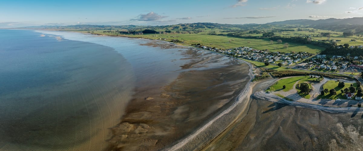 A coastal town with a beach, green fields, and rolling hills in the background.