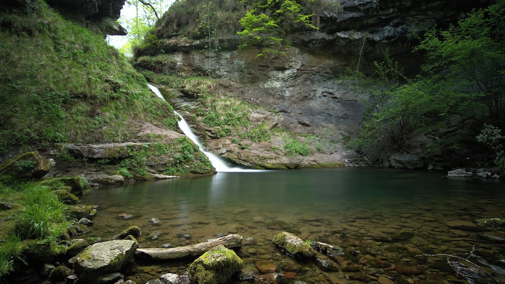 Une cascade se jetant dans un bassin aux eaux limpides, entouré d'un paysage rocheux et d'une végétation luxuriante.