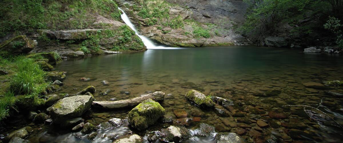A waterfall flowing into a clear pool surrounded by rocky terrain and lush greenery.