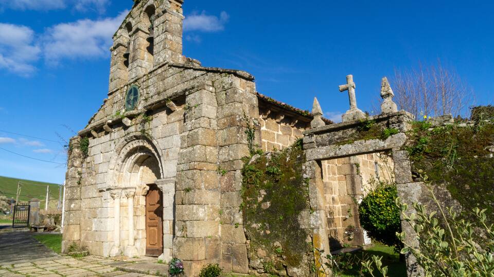 A stone church with a bell tower, arched doorway, and crosses.