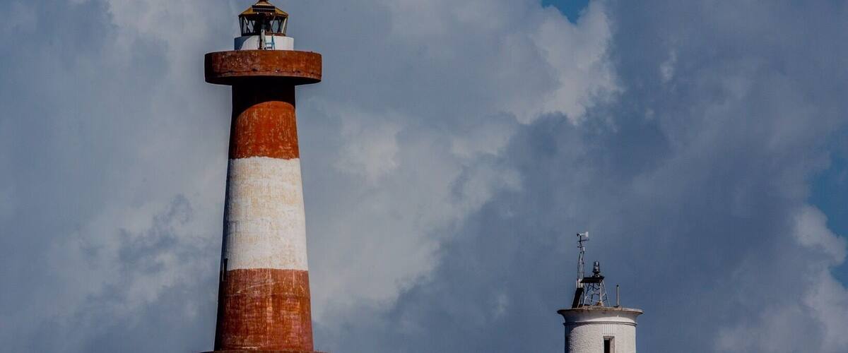 Two lighthouses with red and white stripes against a cloudy sky.