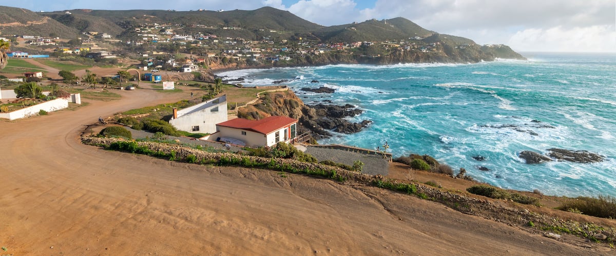A coastal town with a dirt road, houses, and a rocky shoreline.