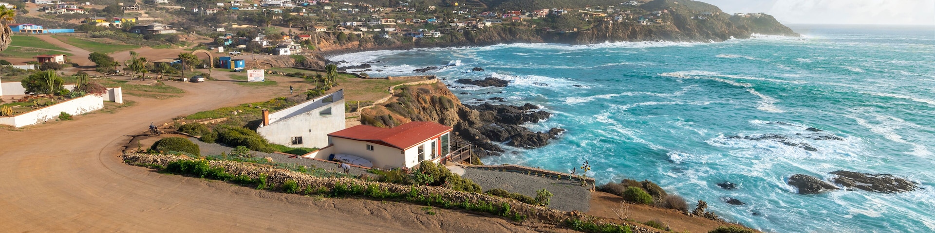 A coastal town with a dirt road, houses, and a rocky shoreline.