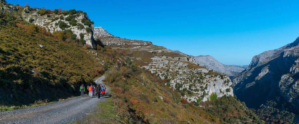 A group of hikers on a gravel road surrounded by mountainous terrain.