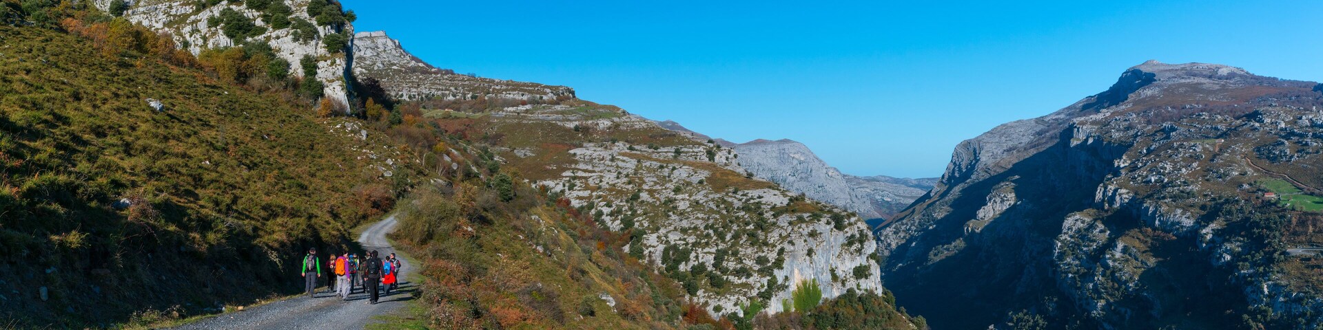 A group of hikers on a gravel road surrounded by mountainous terrain.