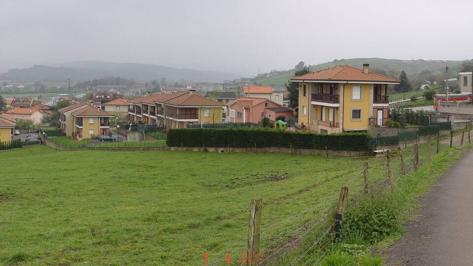 A rural landscape with a road, green fields, and residential buildings.