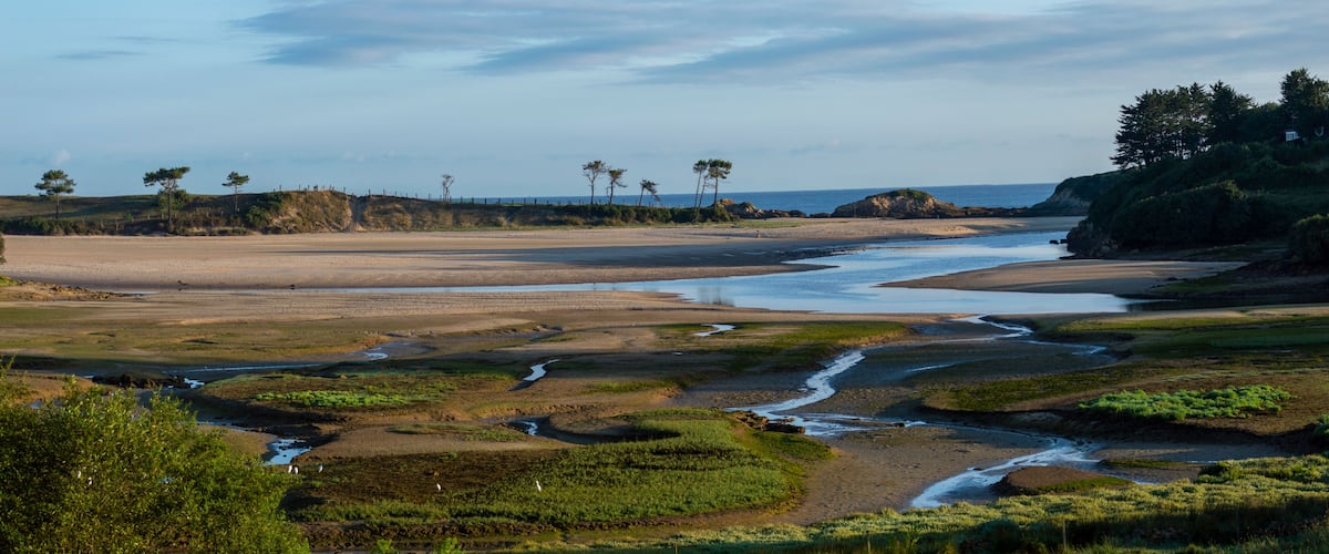A coastal landscape with a river, sandy beach, and sparse vegetation.