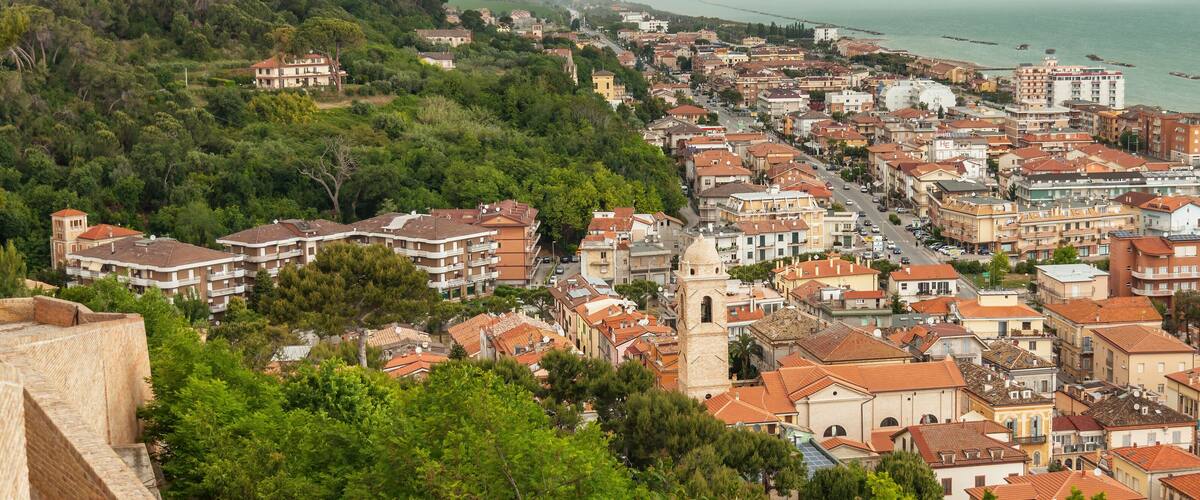A coastal town with dense buildings, a prominent tower, and a beach with boats.