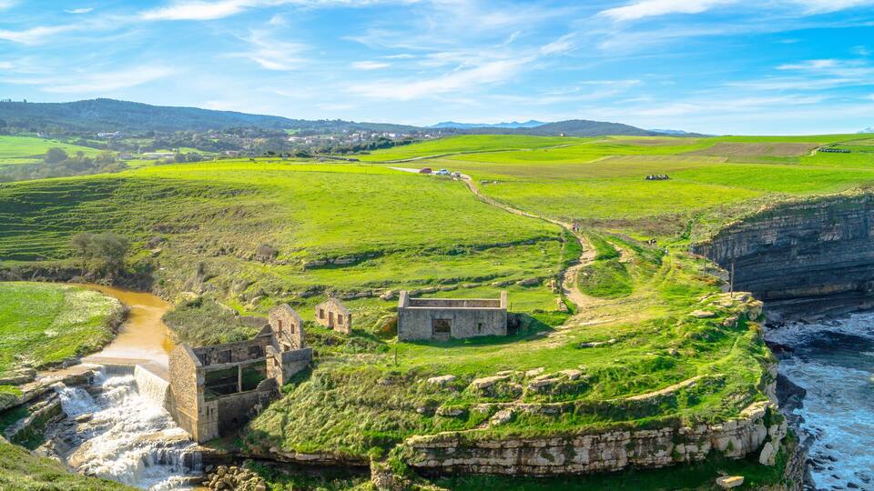 A coastal landscape with a historic stone structure, a river, and green fields.