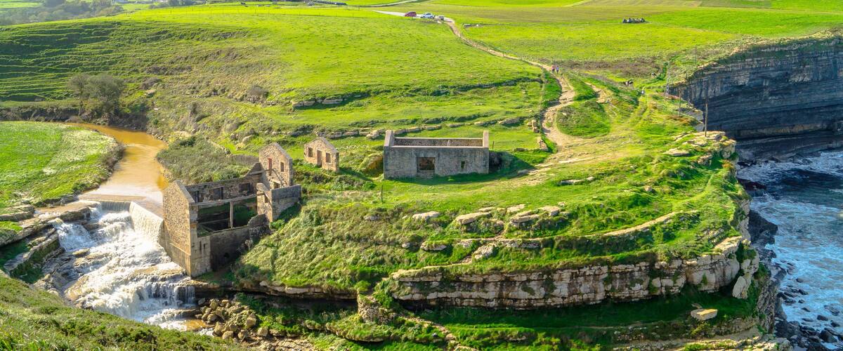 A coastal landscape with a historic stone structure, a river, and green fields.