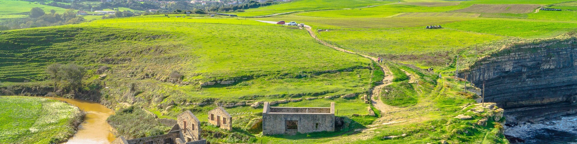 A coastal landscape with a historic stone structure, a river, and green fields.