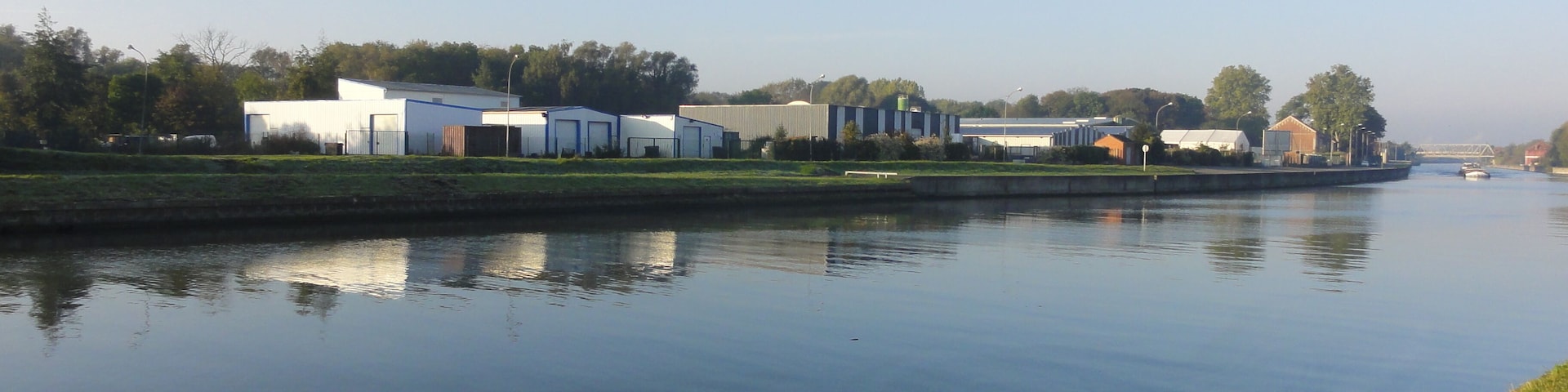 A calm river with industrial buildings and a bridge in the background.