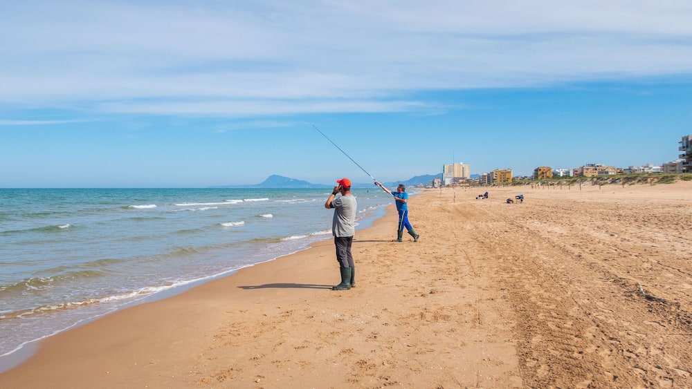 A beach with people fishing and walking along the shore.