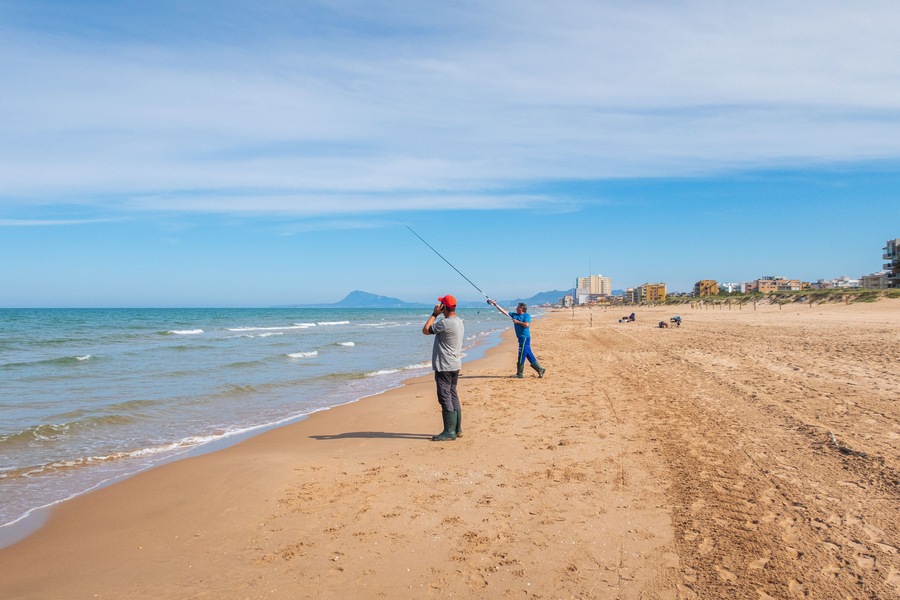 Fisherman throwing the fishing rod, on a beach at sunset, with the Mediterranean sea calm.