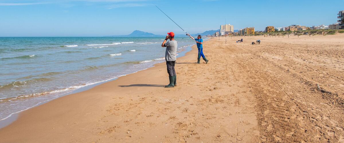 A beach with people fishing and walking along the shore.