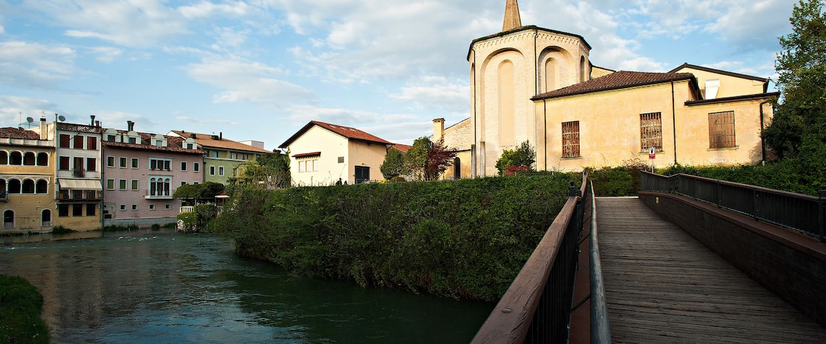 A wooden bridge over a river, with buildings and a church in the background.