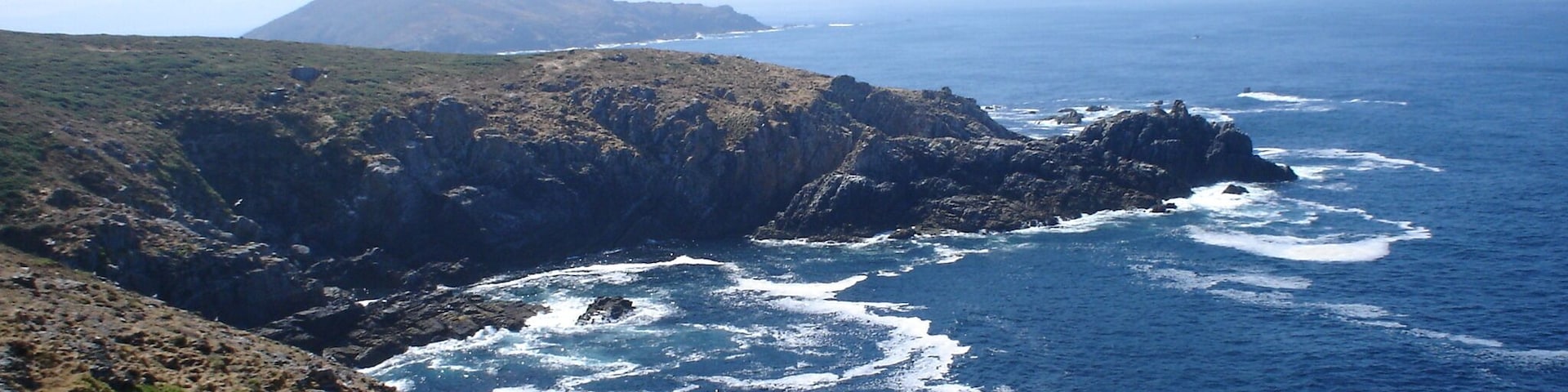 A coastal landscape with rocky cliffs, waves crashing against the shore, and a cross on a rock.