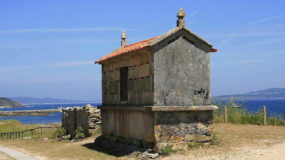 A small stone building with a red-tiled roof near a coastal area.