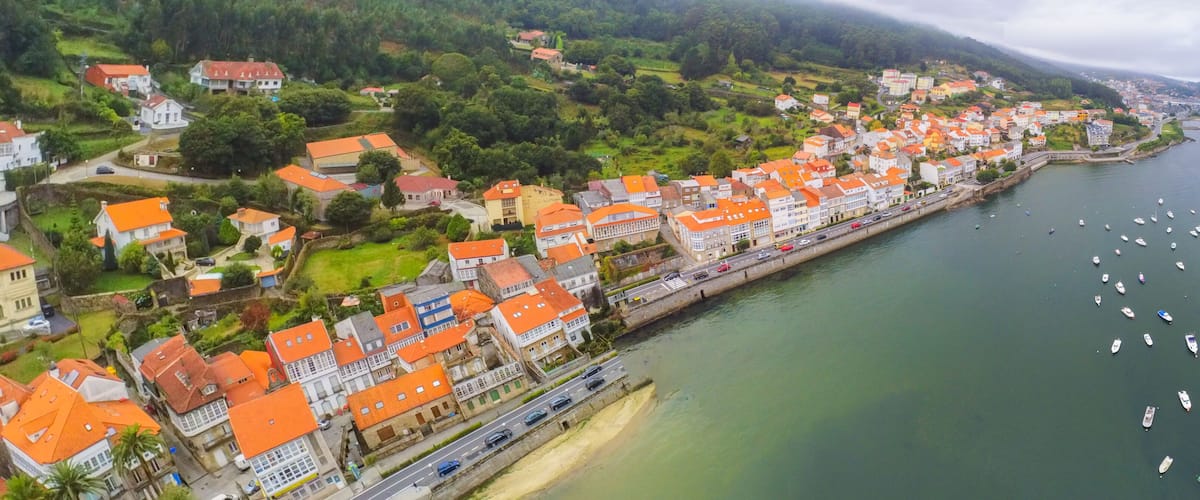 An aerial view of a coastal town with houses along the waterfront, a road parallel to the water, and boats in the sea.