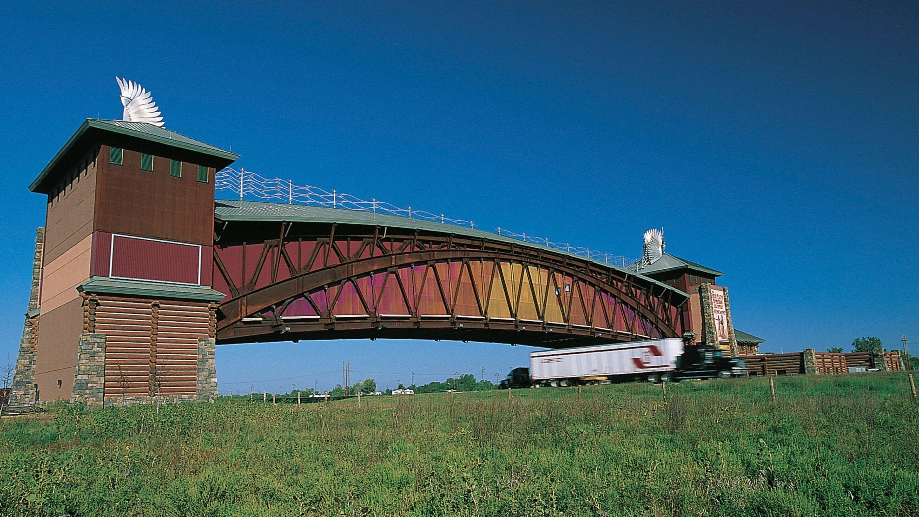 A large metal bridge with decorative wings on top, spanning over a grassy area.