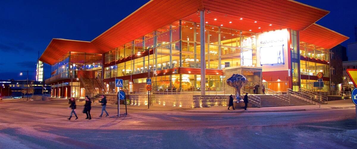 A modern building with a red roof and glass facade, surrounded by a few pedestrians.