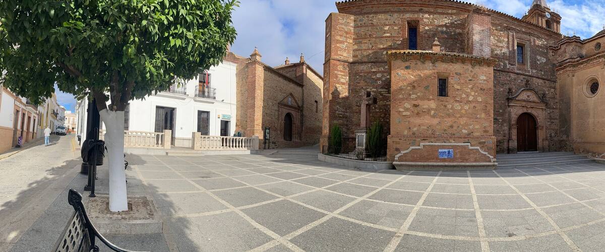 A historic plaza with a central building featuring a round tower and arched doorways.