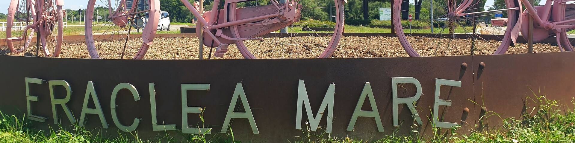 Pink bicycles with pink pelargonium flowers stand at the entrance to the town of Eraclea mare. Panorama.