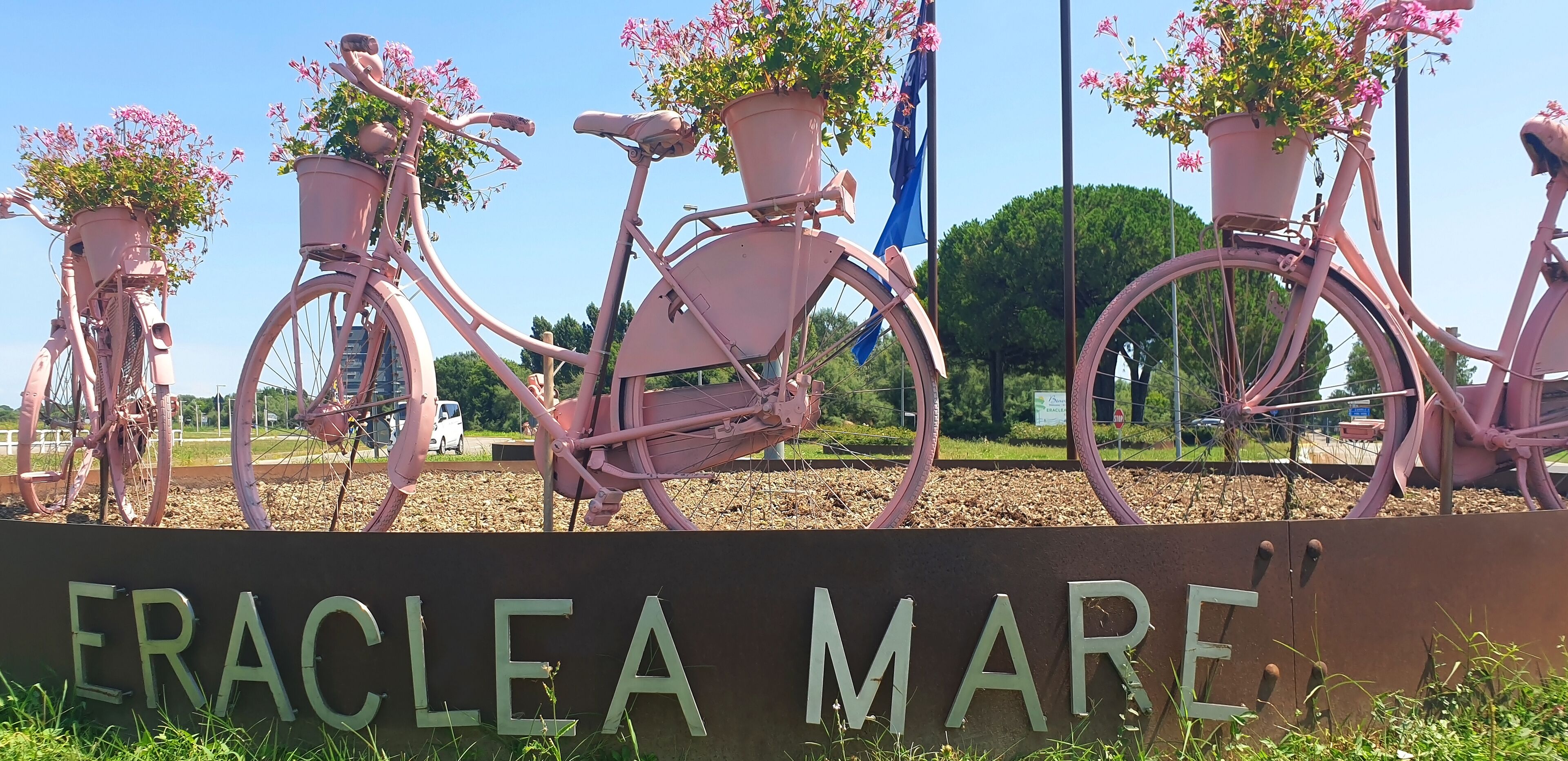 Pink bicycles with potted flowers, a sign reading "ERACLEA MARE," and a clear blue sky.