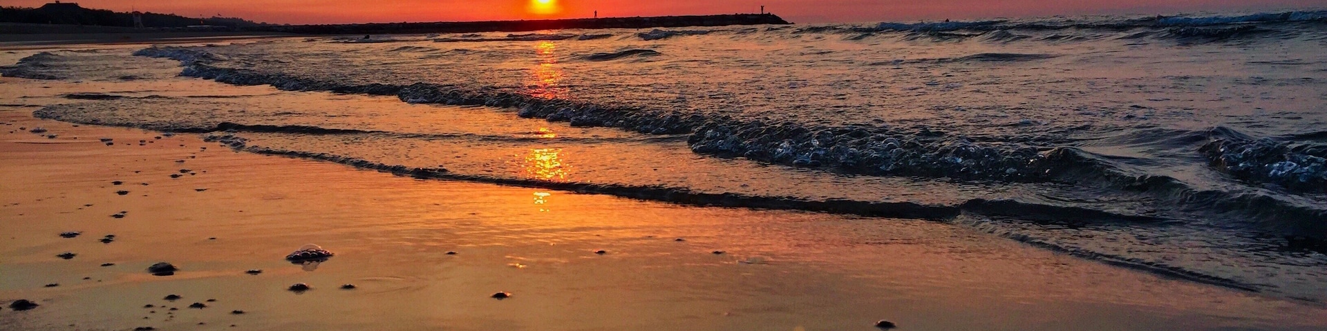 Un atardecer sobre una playa con olas mansas acariciando la orilla.