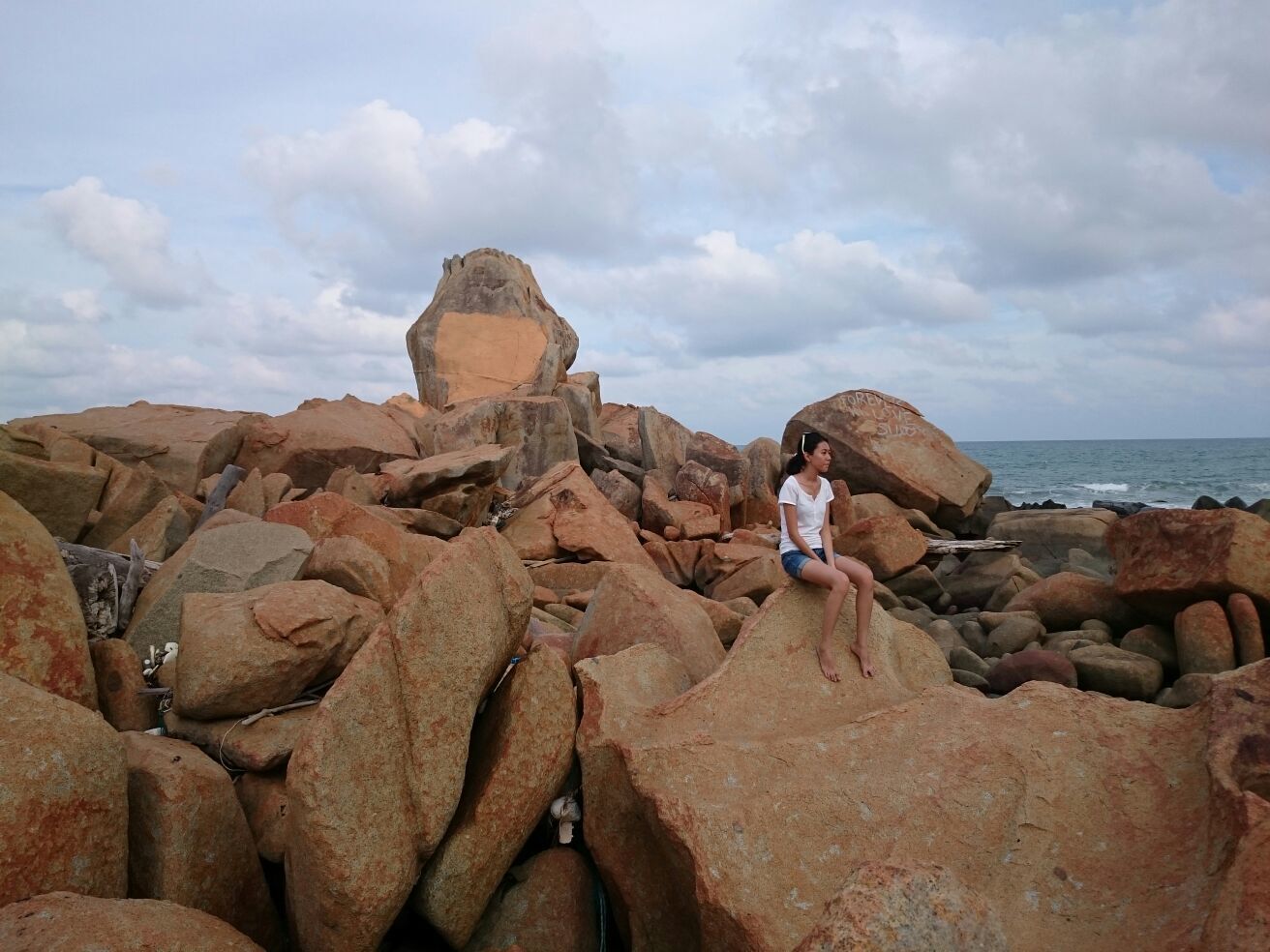 A rocky beach with large boulders and a person sitting on one of the rocks.