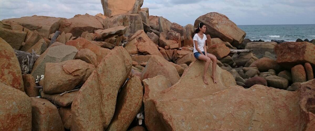 A rocky beach with large boulders and a person sitting on one of the rocks.