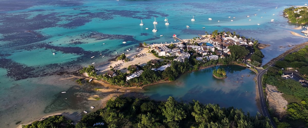 An aerial view of a coastal town with a small island, clear turquoise waters, and several boats.