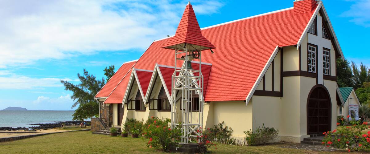 A church with a red roof and white walls by the sea.