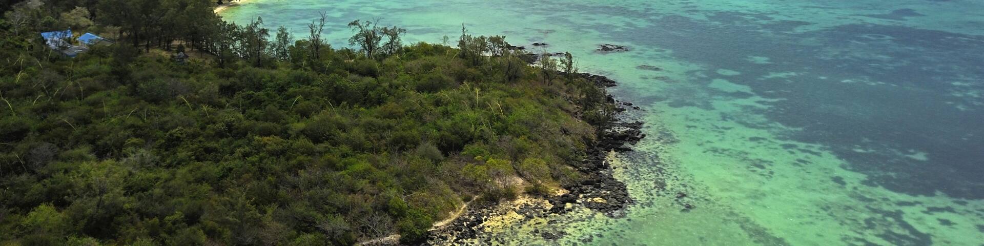 A tropical island landscape with clear turquoise waters, dense greenery, and a distant island.