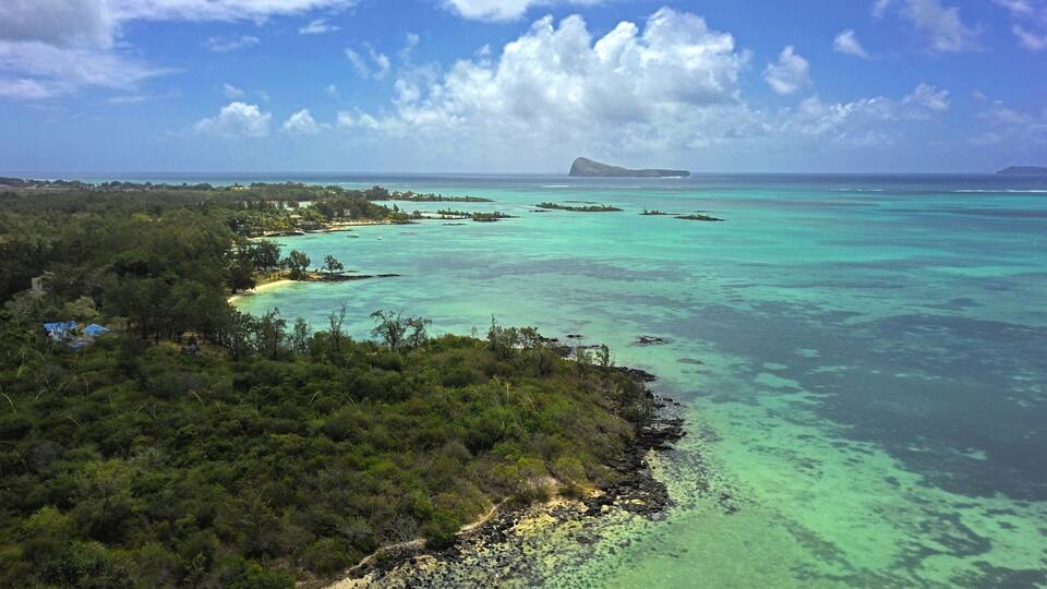 A tropical island landscape with clear turquoise waters, dense greenery, and a distant island.