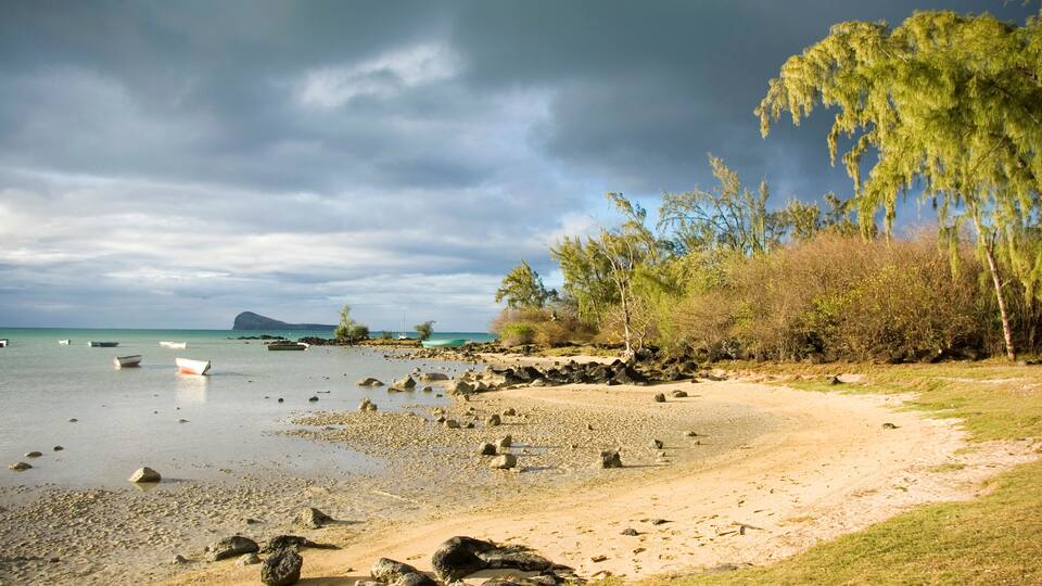A beach with scattered rocks, calm water, and boats.