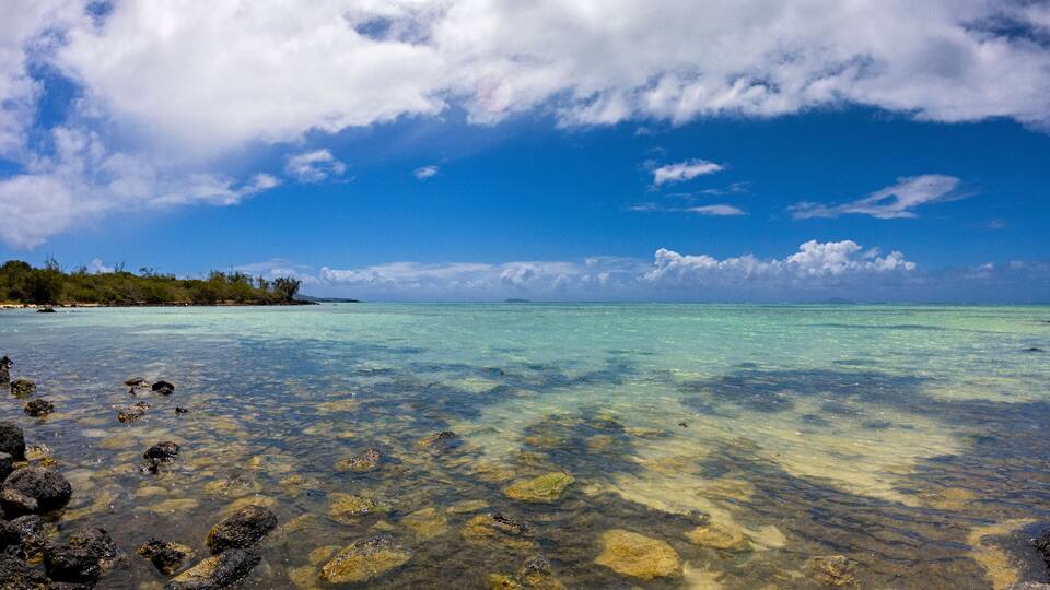 A clear turquoise sea with visible rocks and a distant shoreline with trees.