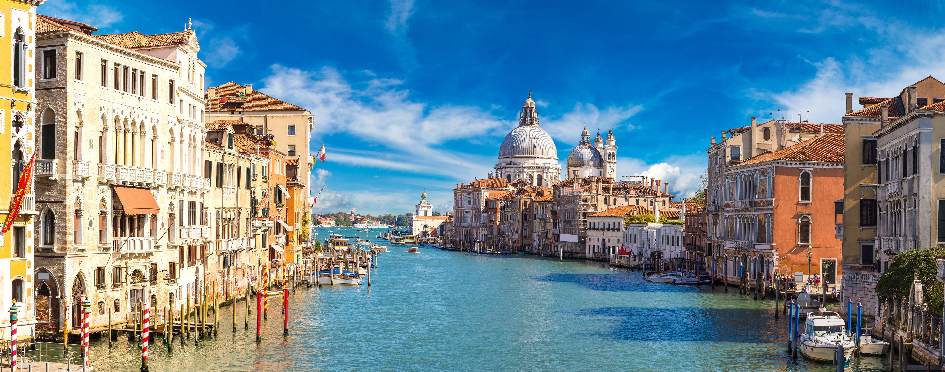 A canal in Venice with historic buildings, a prominent dome, and boats.