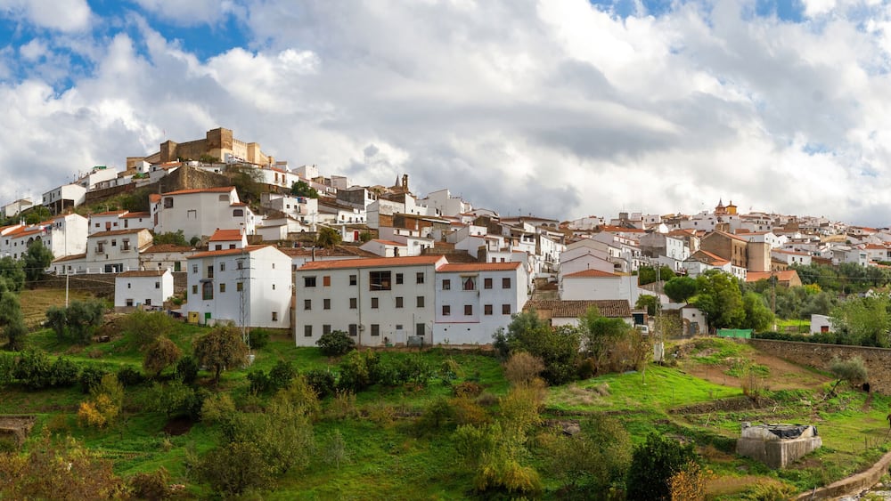 A hillside town with white buildings, a stone bridge, and a river.