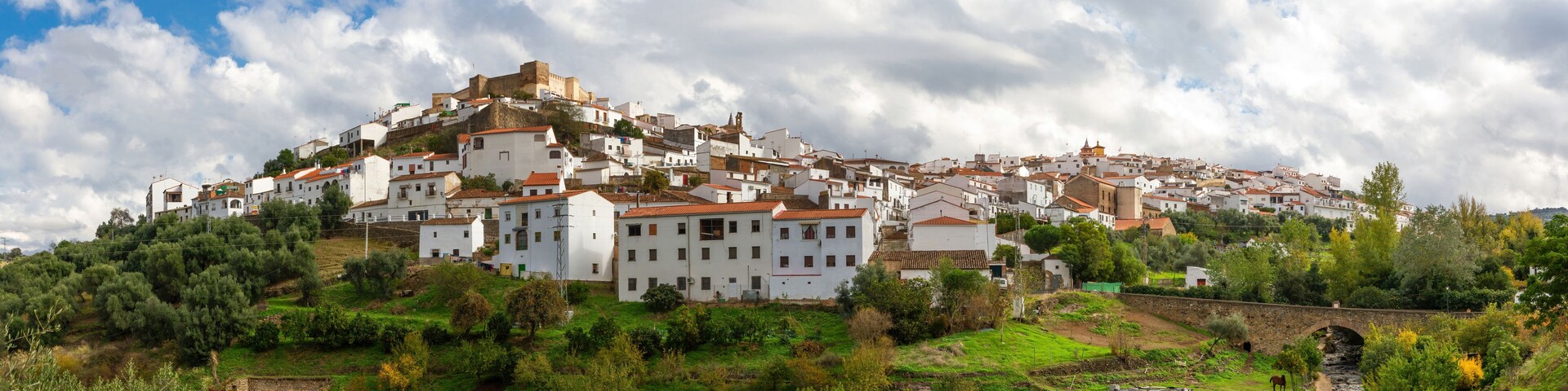 A hillside town with white buildings, a stone bridge, and a river.