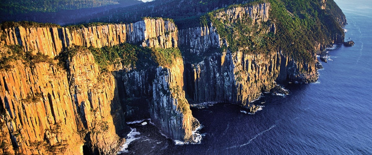 A coastal cliff with steep, vertical rock faces and a narrow beach at the base.