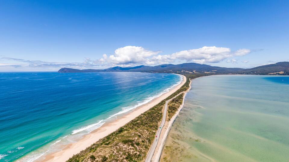 A coastal landscape with a sandy beach, a clear blue ocean, and a winding road along the shore.