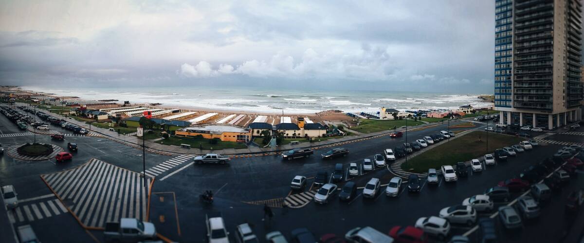A coastal cityscape with a beach, parking lots, and a tall building.