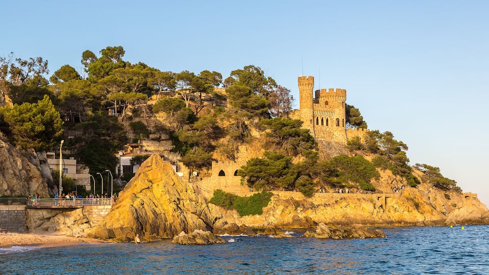 A coastal castle on a rocky cliff with a bridge leading to it.